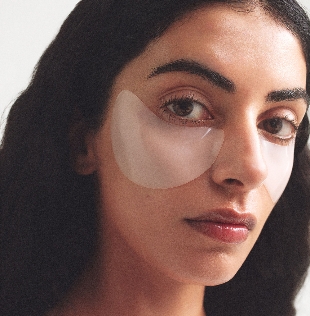Woman with long dark hair wearing translucent Night Night Eye Patches under her eyes