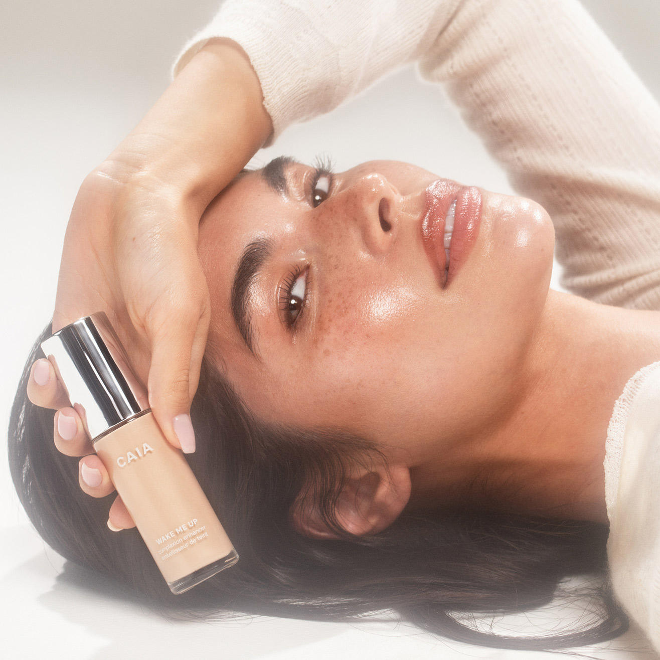Woman wearing wake me up complexion enhancer and holding the bottle